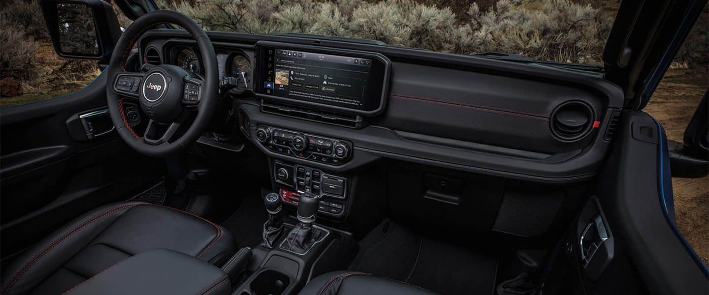 The interior of the 2021 Jeep Wrangler Sahara focusing on the steering wheel, entertainment center and dashboard.
