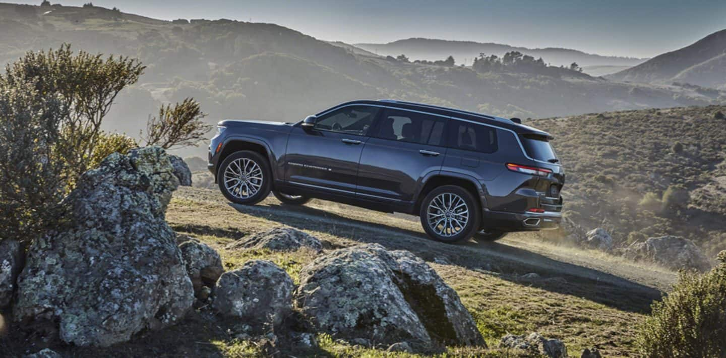 The 2022 Jeep Grand Cherokee Trailhawk being driven off-road, with both front wheels elevated as it is driven over rocks.