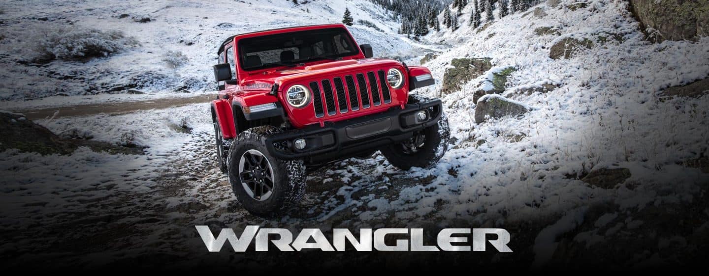 A red 2022 Jeep Wrangler Rubicon crawling over a snow-covered rocky hill off-road. Wrangler.