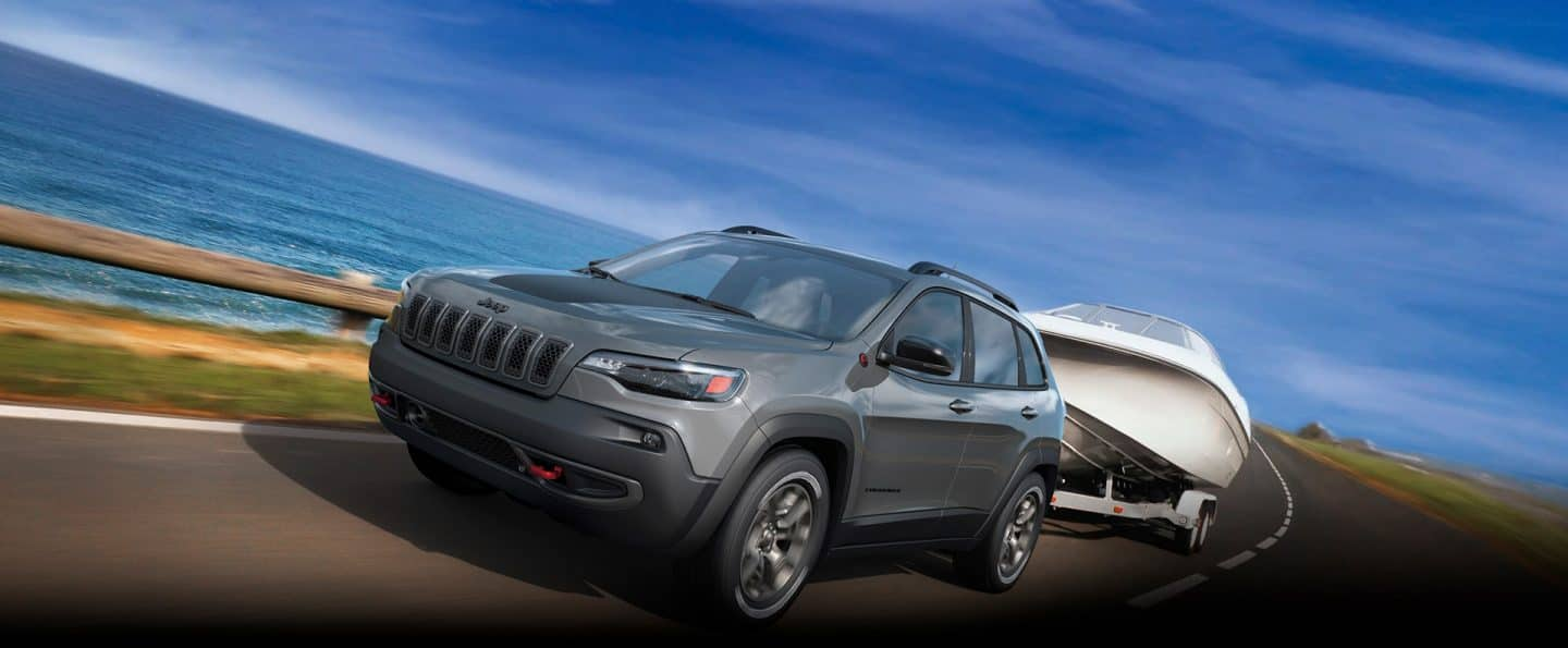 Un Jeep Cherokee Trailhawk 2023 gris circulando en una autopista al costado del mar y remolcando una lancha.