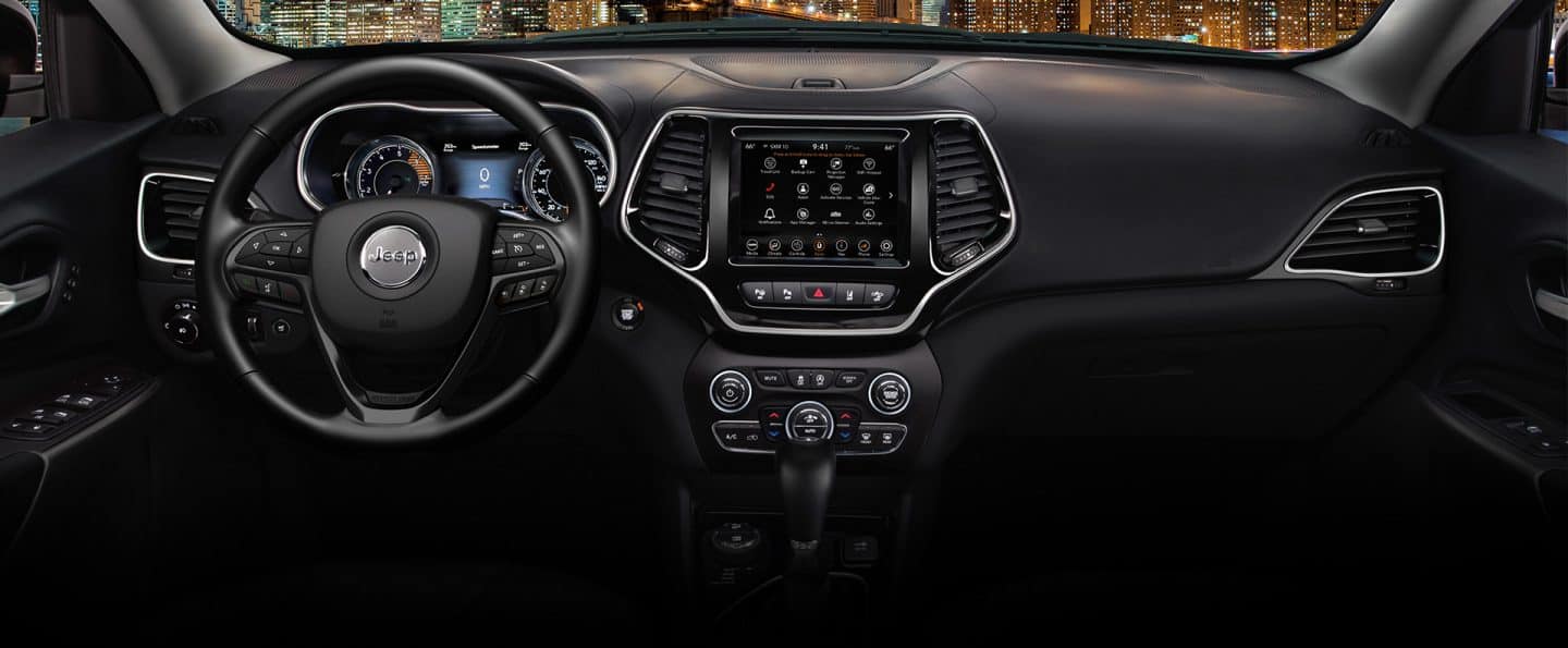 Interior del Jeep Cherokee Altitude Lux 2023, donde se destacan el volante, la pantalla digital situada en el panel de instrumentos, la pantalla táctil Uconnect y los controles de la consola central.