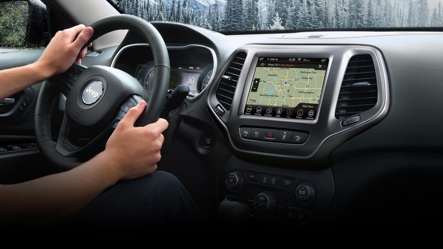 Interior del Jeep Cherokee 2023, donde se destacan el volante, el panel de instrumentos y la pantalla táctil Uconnect, y la pantalla táctil muestra una amplia variedad de opciones de menú.