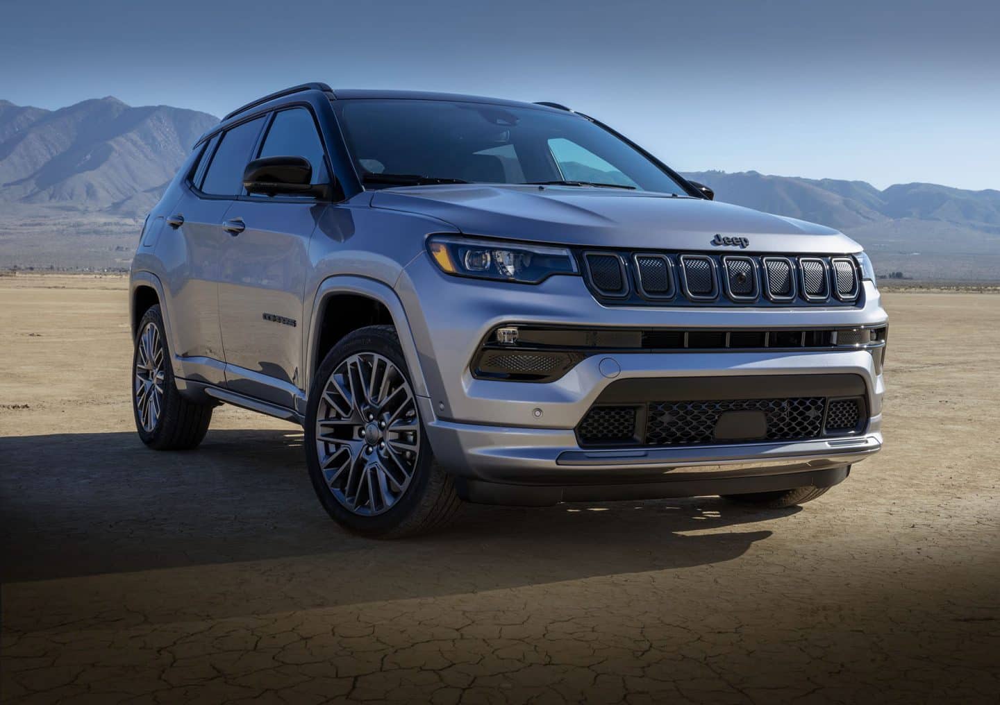 The 2023 Jeep Compass High Altitude parked on a dry, desert-like surface, with mountains in the distant background. 