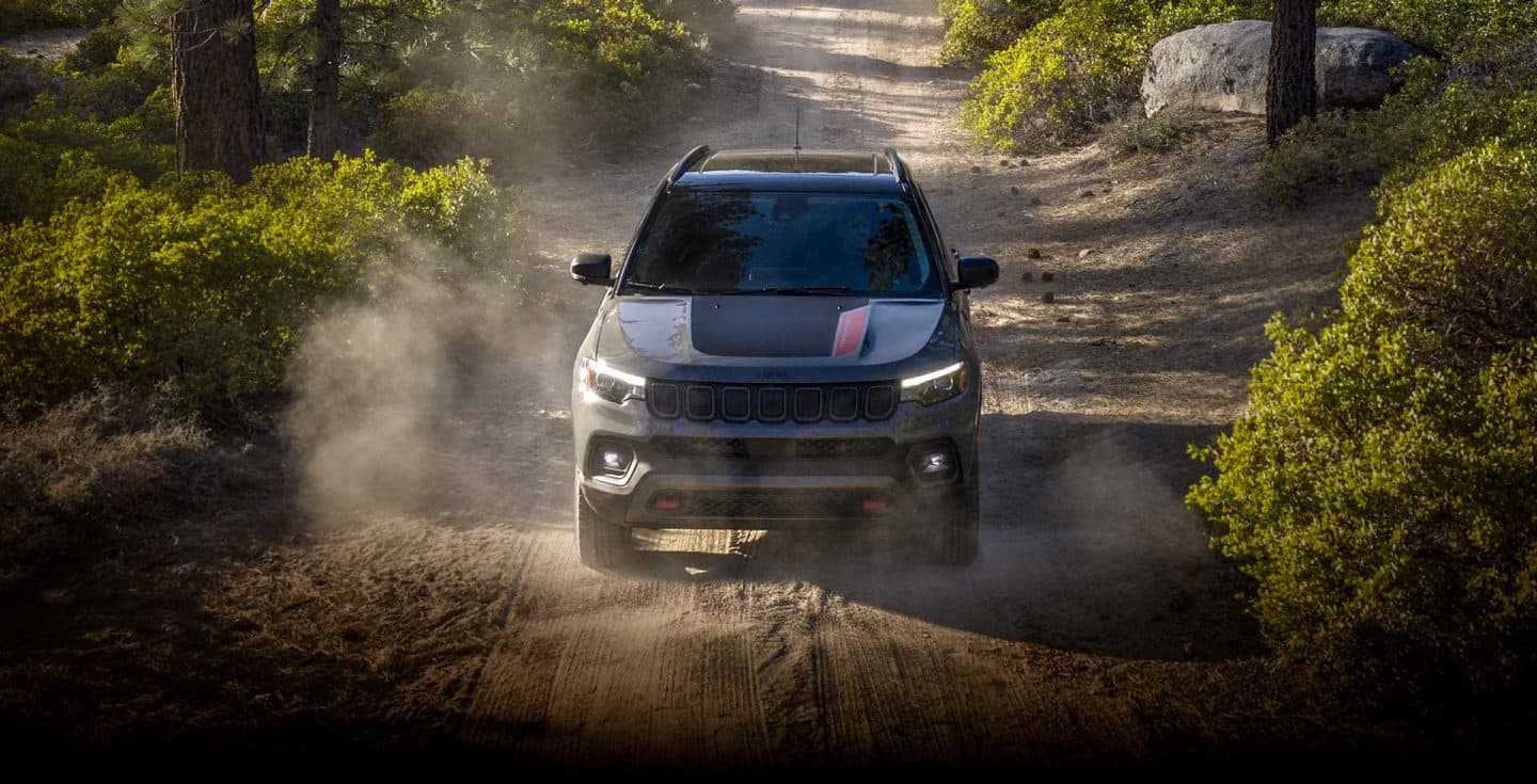 A raised head-on view of a 2023 Jeep Compass Trailhawk being driven off-road through a wooded trail.