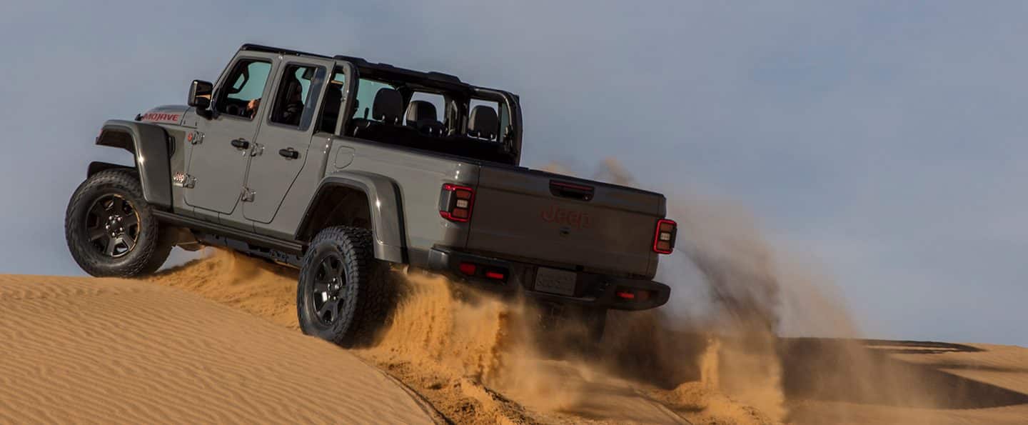 The 2023 Jeep Gladiator Mojave parked on a hill with the sunset reflected on its driver-side doors.