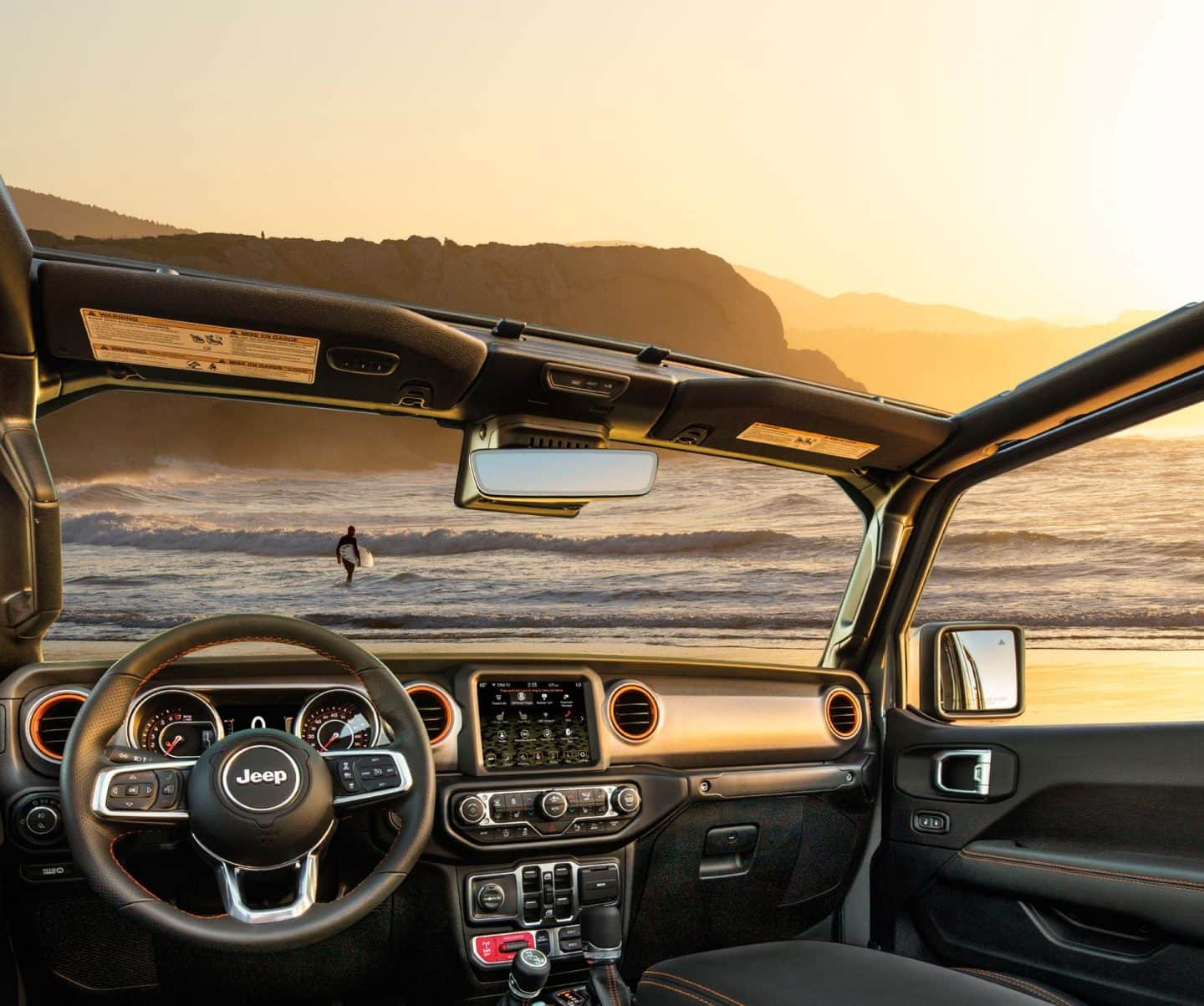 El interior de la Jeep Gladiator Mojave 2023 sin el techo, con un primer plano del océano y el cielo que se ven por el parabrisas, y el techo y las ventanillas abiertas.