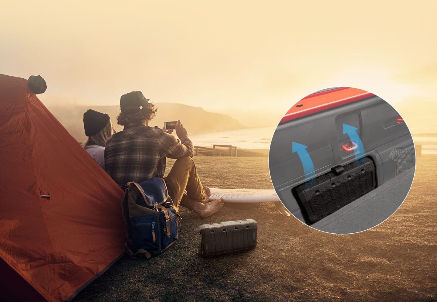 A couple camping on the beach with the man holding a smartphone with an available Bluetooth speaker on the ground beside him. Inset image of the Bluetooth speaker in its charging port in the 2023 Jeep Gladiator.