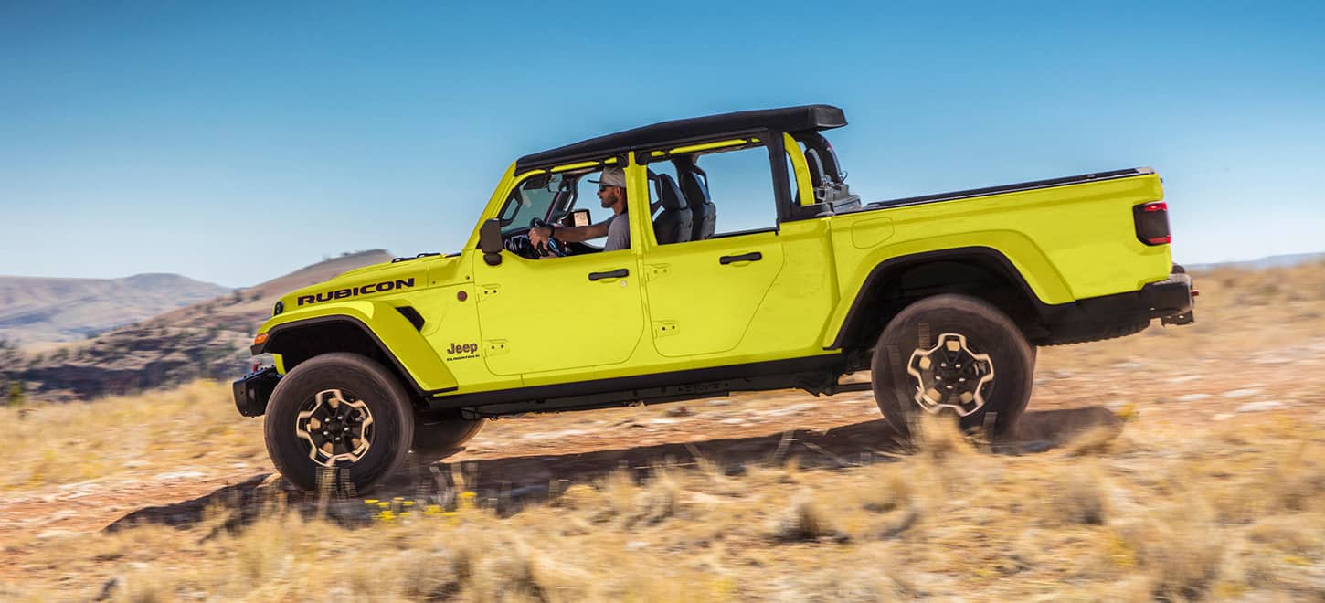 A profile view of a yellow 2023 Jeep Gladiator Rubicon with half doors, being driven down a hill.