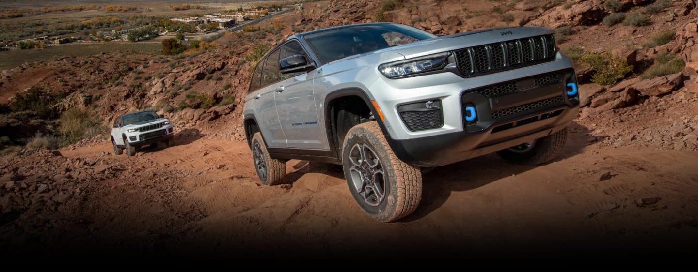 The 2023 Jeep Grand Cherokee 4xe climbing up a steep mountain trail with another Grand Cherokee 4xe following.