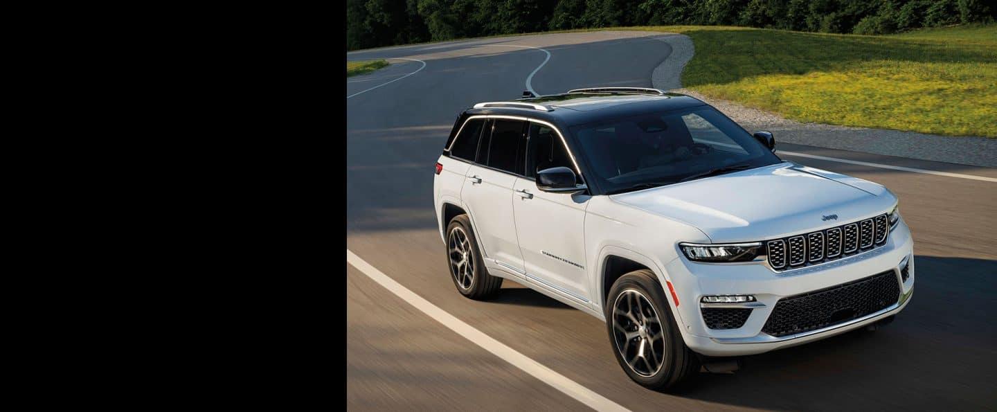 A white 2023 Jeep Grand Cherokee Summit Reserve being driven on a winding road.