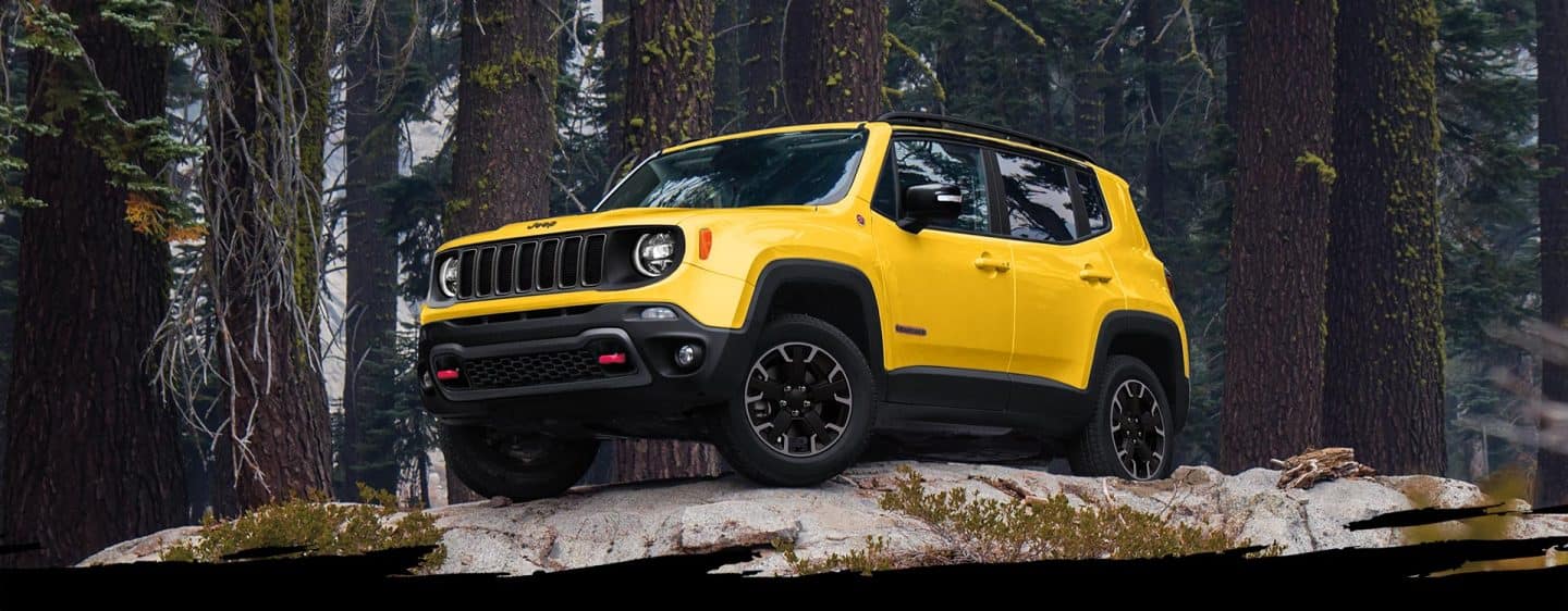 Un Jeep Renegade Trailhawk 2023 amarillo estacionado sobre roca lisa, con árboles de fondo.