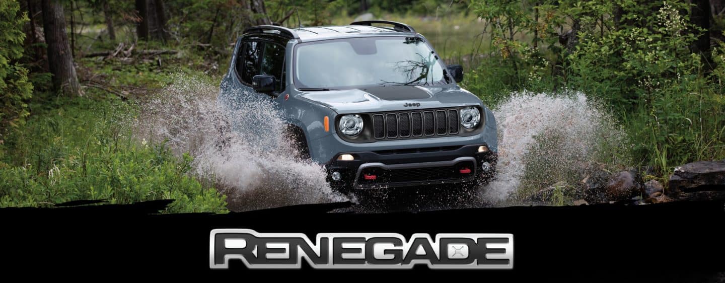 A blue gray 2023 Jeep Renegade Trailhawk fording through a narrow creek off-road, with water spraying above the vehicle's wheel wells. Renegade.