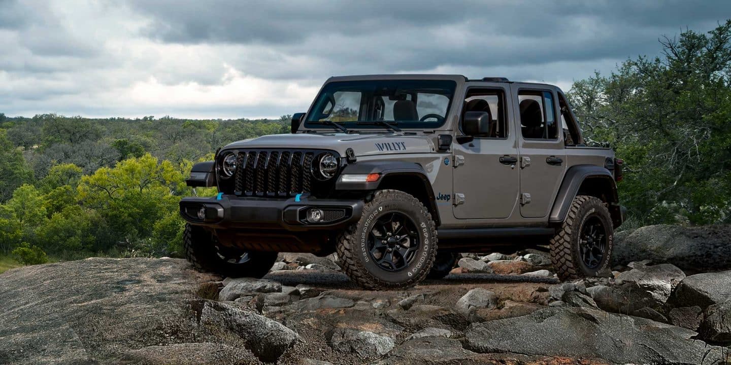 Un Jeep Wrangler Willys 4xe 2023 estacionado sobre una saliente rocosa, con un cielo tormentoso por encima y un bosque por debajo.