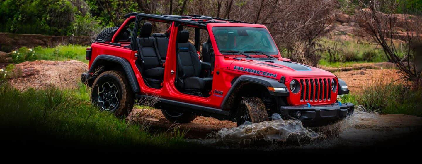 The 2023 Jeep Wrangler Rubicon 4xe being driven through a shallow stream with its doors and roof off.