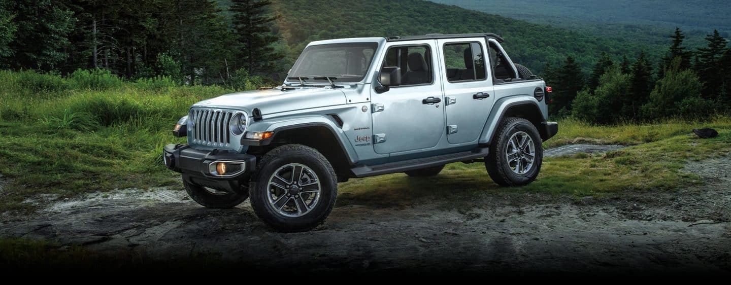 Un Jeep Wrangler Sahara 2023 estacionado fuera de la carretera en un pedazo de tierra desnuda, rodeado de césped y árboles.