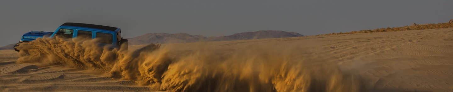 The 2023 Jeep Wrangler Rubicon 392 being driven off-road on sand, with a billowing cloud of dust obscuring most of the vehicle.