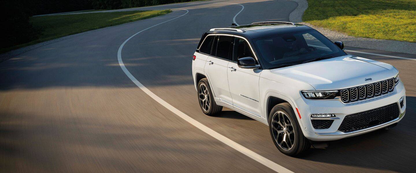 Un Jeep Grand Cherokee Summit Reserve alb din 2024, condus pe o autostradă curbată.
