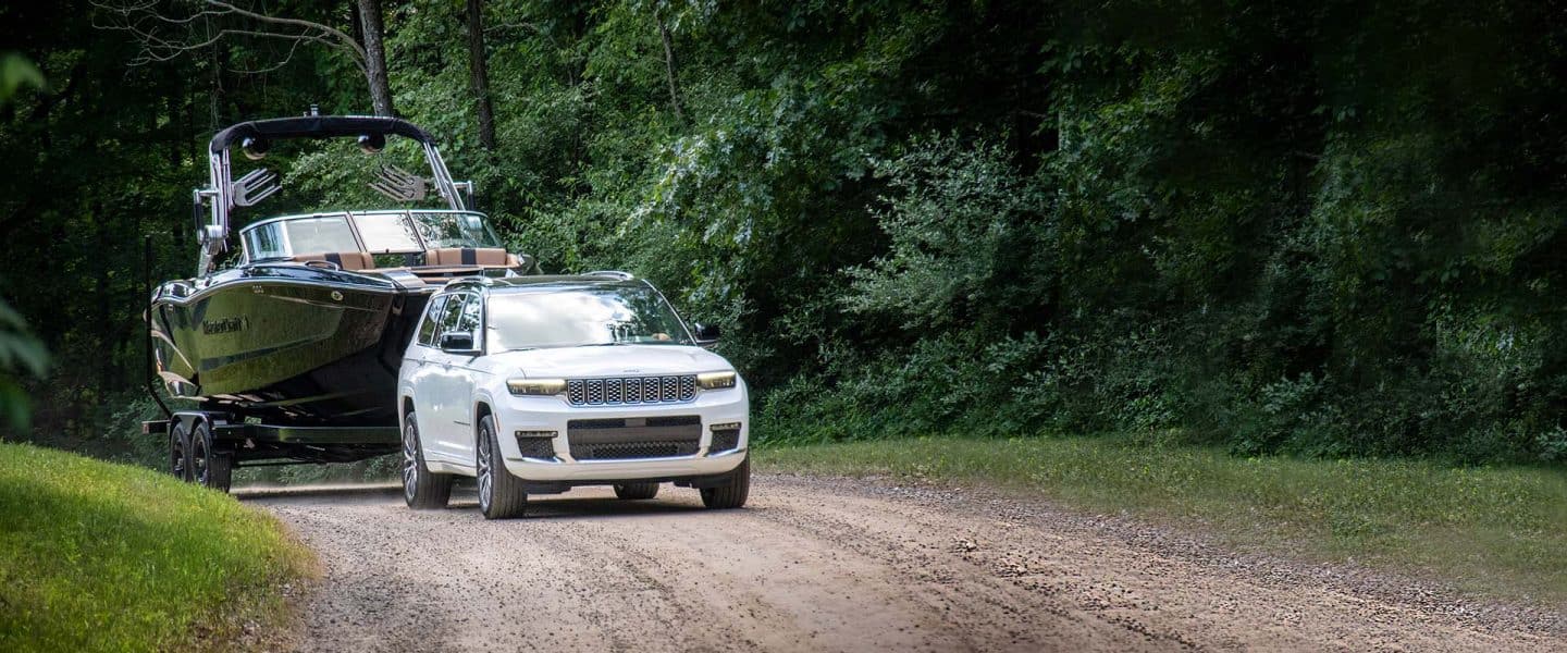 Un Jeep Grand Cherokee Summit Reserve alb din 2024 condus pe un drum murdar în timp ce tracta o barcă cu motor.