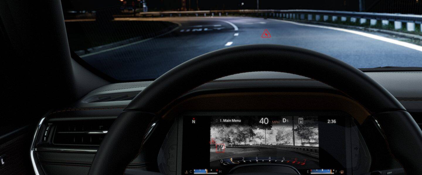Interiorul Jeep Grand Cherokee 2024 din perspectiva șoferului, demonstrând prin parbriz că vehiculul este condus pe o autostradă în întuneric, deoarece Clusterul Digital al Informațiilor despre Șoferi afișează o imagine nocturnă a drumului din față, dezvăluind o căprioară lângă carosabil.