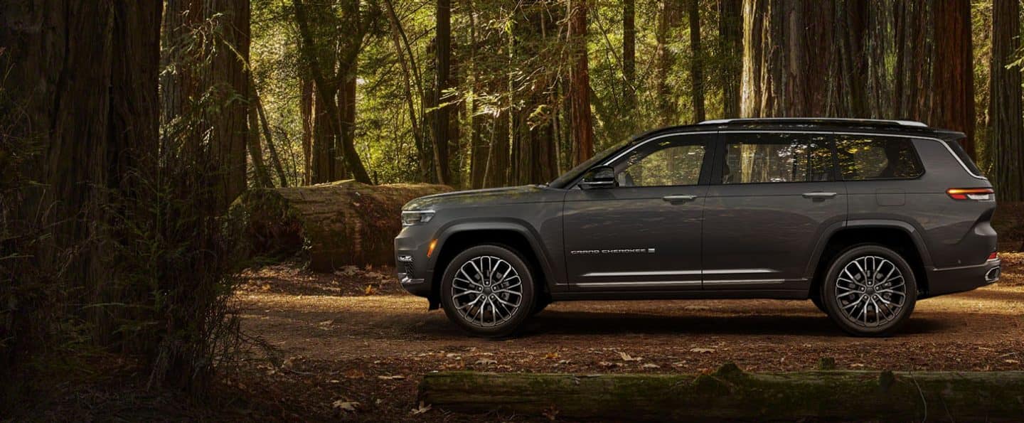 El perfil del lado del conductor de un Jeep Grand Cherokee L Summit Reserve 2024 estacionado en un bosque.