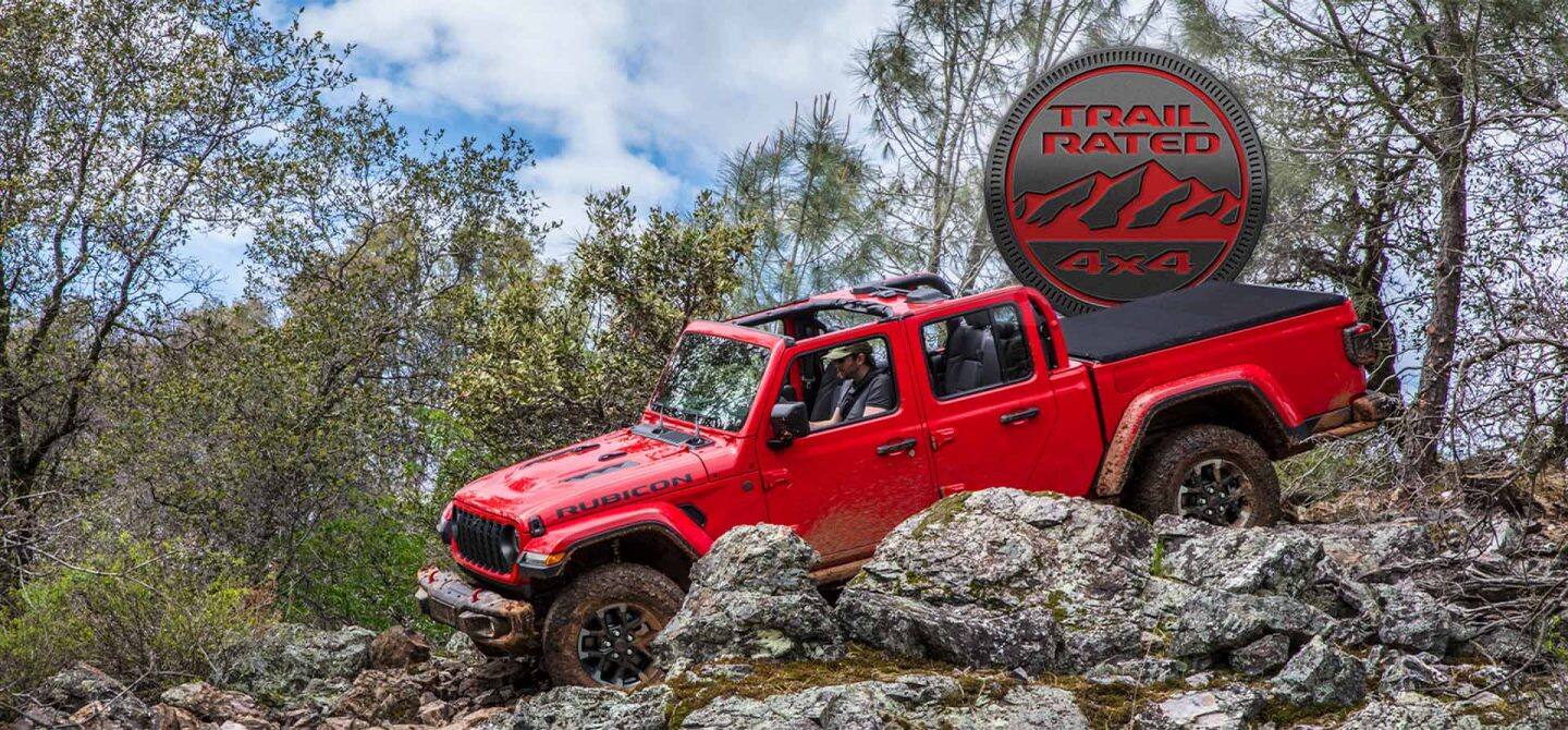 Un Jeep Gladiator Rubicon X rojo de 2025 con su techo retirado, gateando sobre una serie de rocas y afloramientos fuera de carretera. Emblema Trail Rated 4x4.
