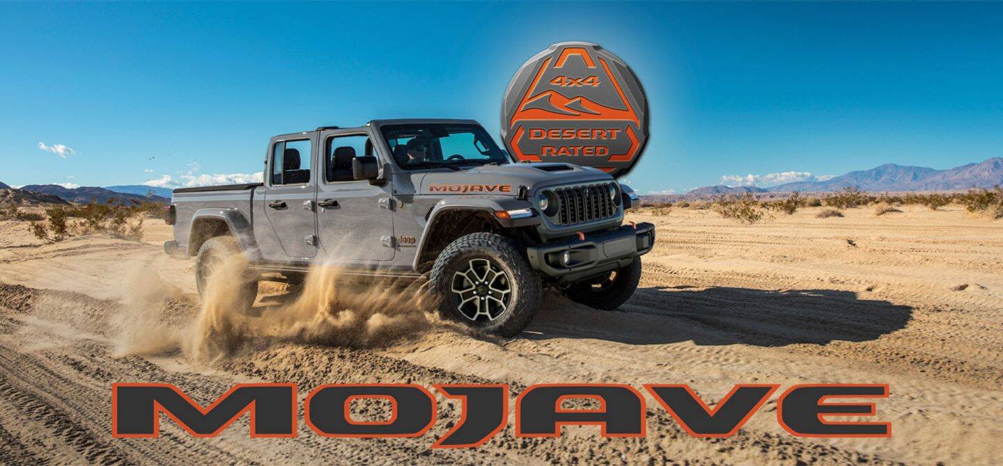 Un Jeep Gladiator Mojave X gris de 2025 que atraviesa el desierto y levanta el polvo a medida que avanza. El emblema 4x4 de Desert Rated. Mojave.