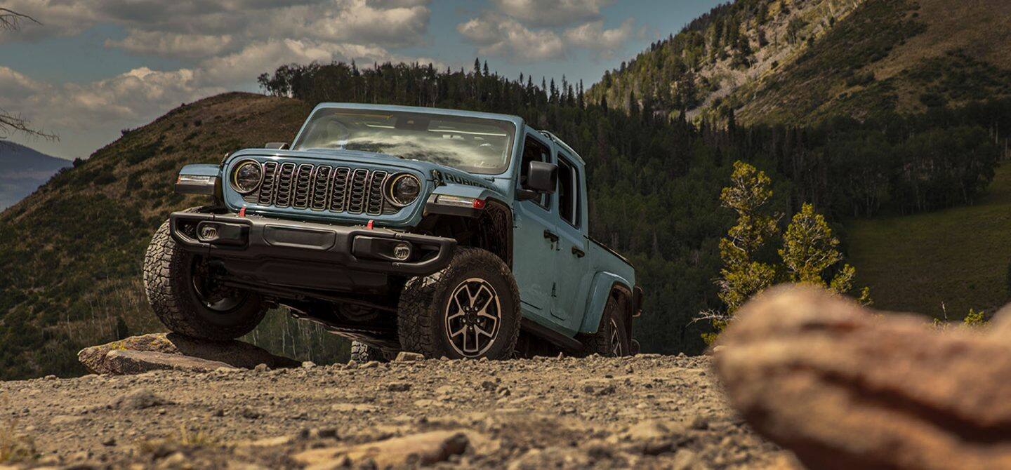 Un Jeep Gladiator Rubicon X rojo de 2025 ascendiendo por un sendero escarpado y rocoso todoterreno, con un Jeep Gladiator Rubicon X verde oliva de 2025 detrás.