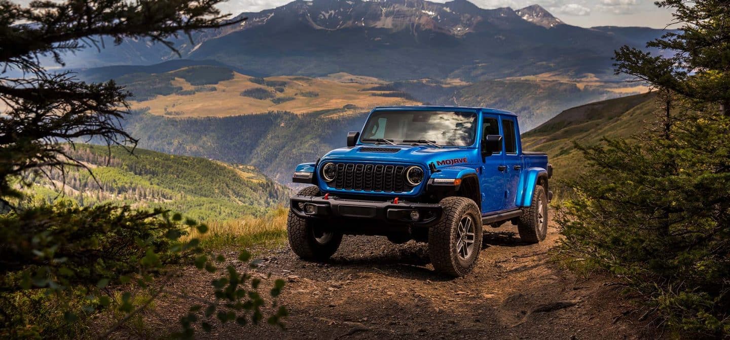Un Jeep Gladiator Mojave X azul de 2025 estacionado en un despeje en las montañas.