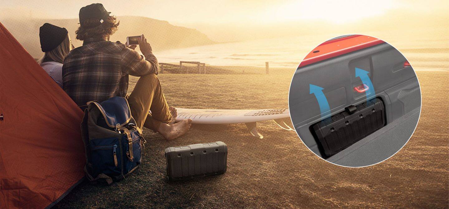 Una pareja sentada en una playa junto a una tienda, un altavoz inalámbrico extraíble junto a ellos en la arena. Se muestra una imagen insertada en la que el altavoz encaja en el lateral de la plataforma del Jeep Gladiator camión de 2025.
