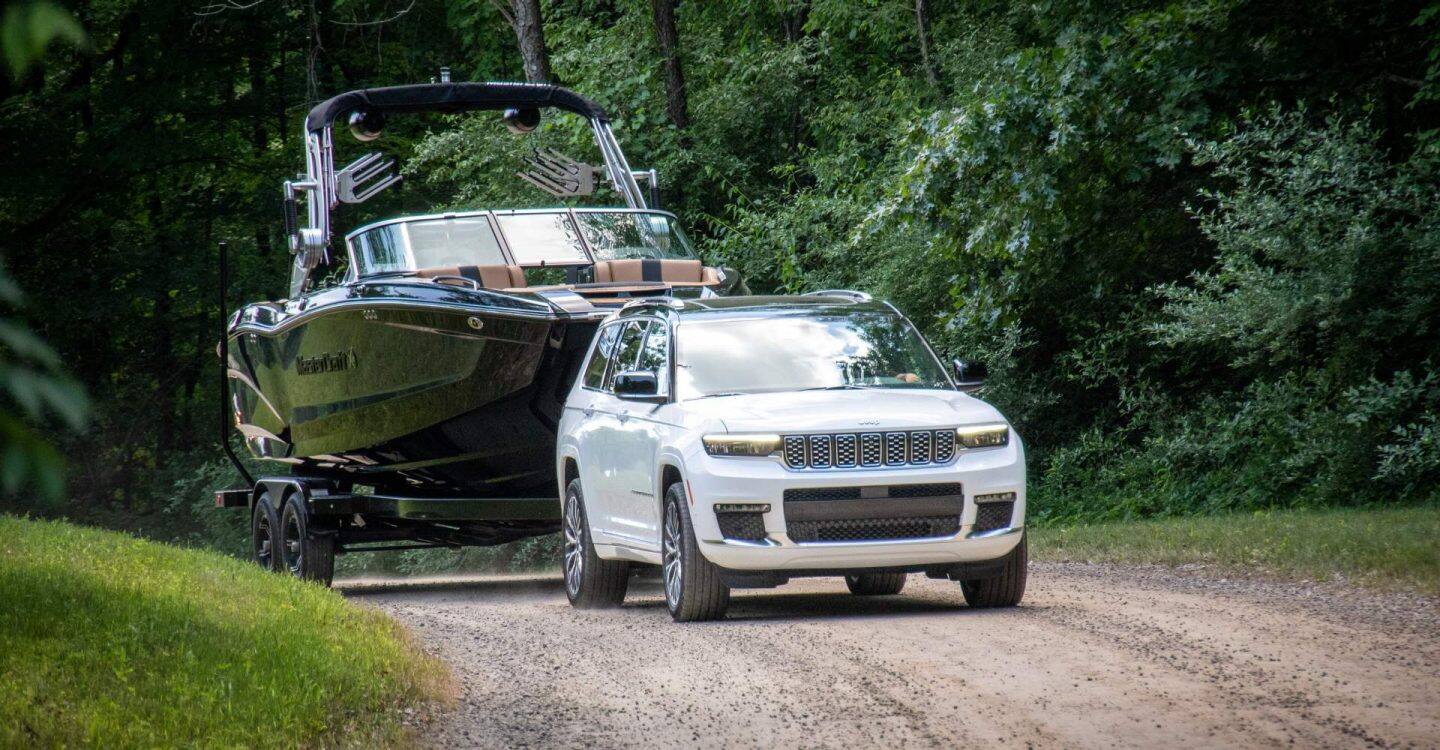Un Jeep Grand Cherokee Summit Reserve 2025 blanco circulando por un camino de tierra, remolcando una lancha a motor de gran tamaño.