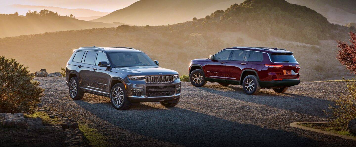 Tres modelos Grand Cherokee 2025 estacionados en un claro rocoso al anochecer, con las montañas al fondo; De izquierda a derecha: un Grand Cherokee Overland gris, un Grand Cherokee Summit blanco y un Grand Cherokee Trailhawk 4xe plateado con capó negro.