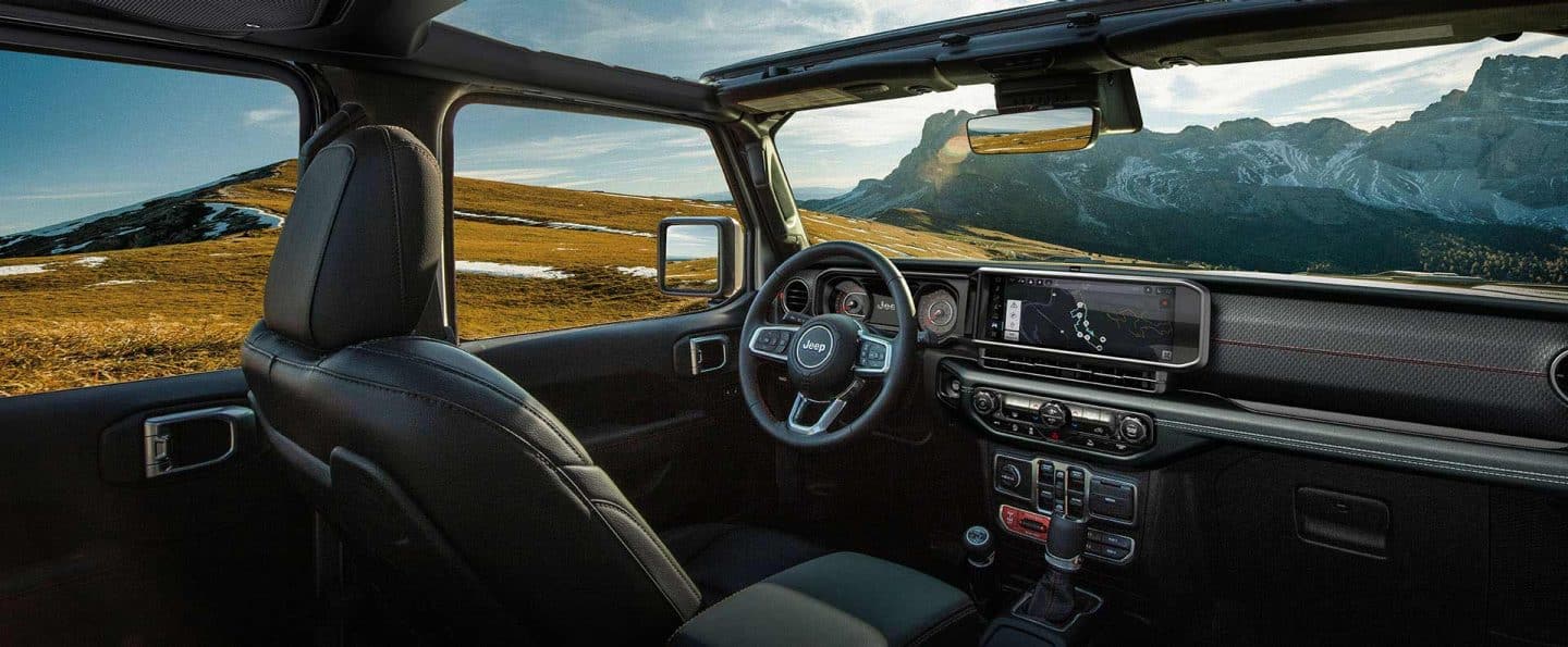 La primera fila del 2025 Jeep Wrangler se centra en el techo solar abierto, el volante, la Uconnect pantalla táctil y el salpicadero.