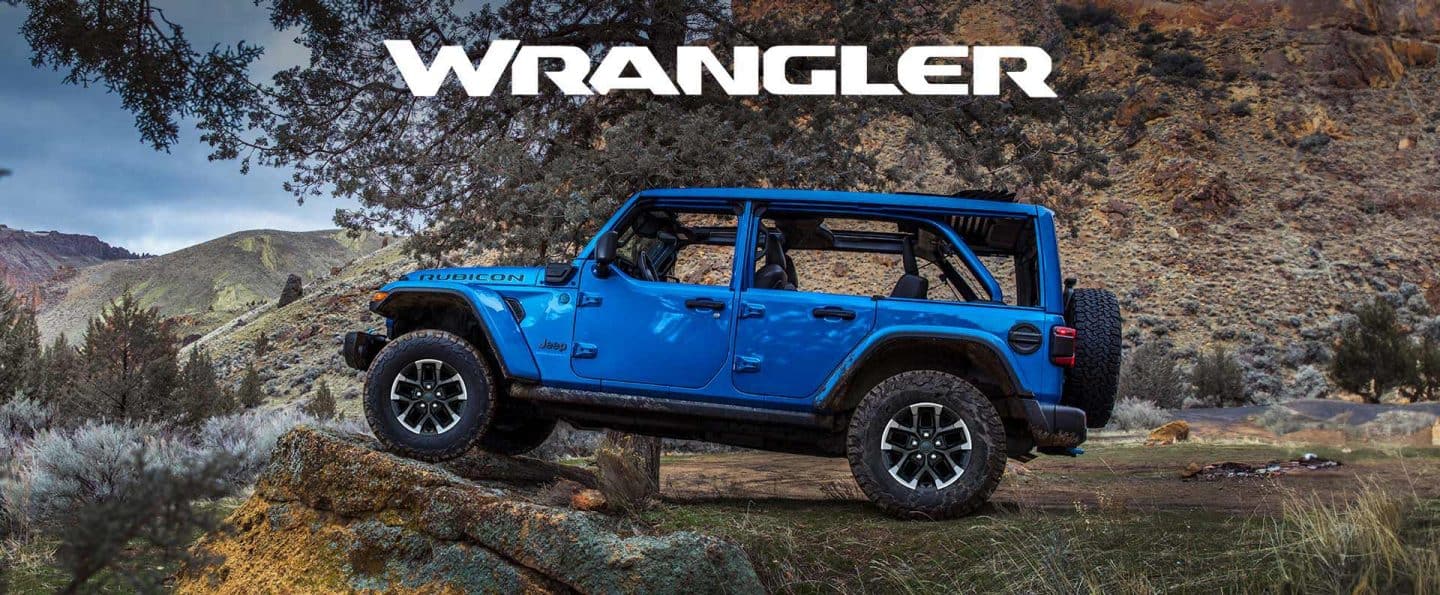 Un perfil del lado del conductor de un Jeep Wrangler Rubicon X 4xe azul 2025 aparcado fuera de carretera, con sus neumáticos delanteros elevados en una formación rocosa elevadaWrangler.