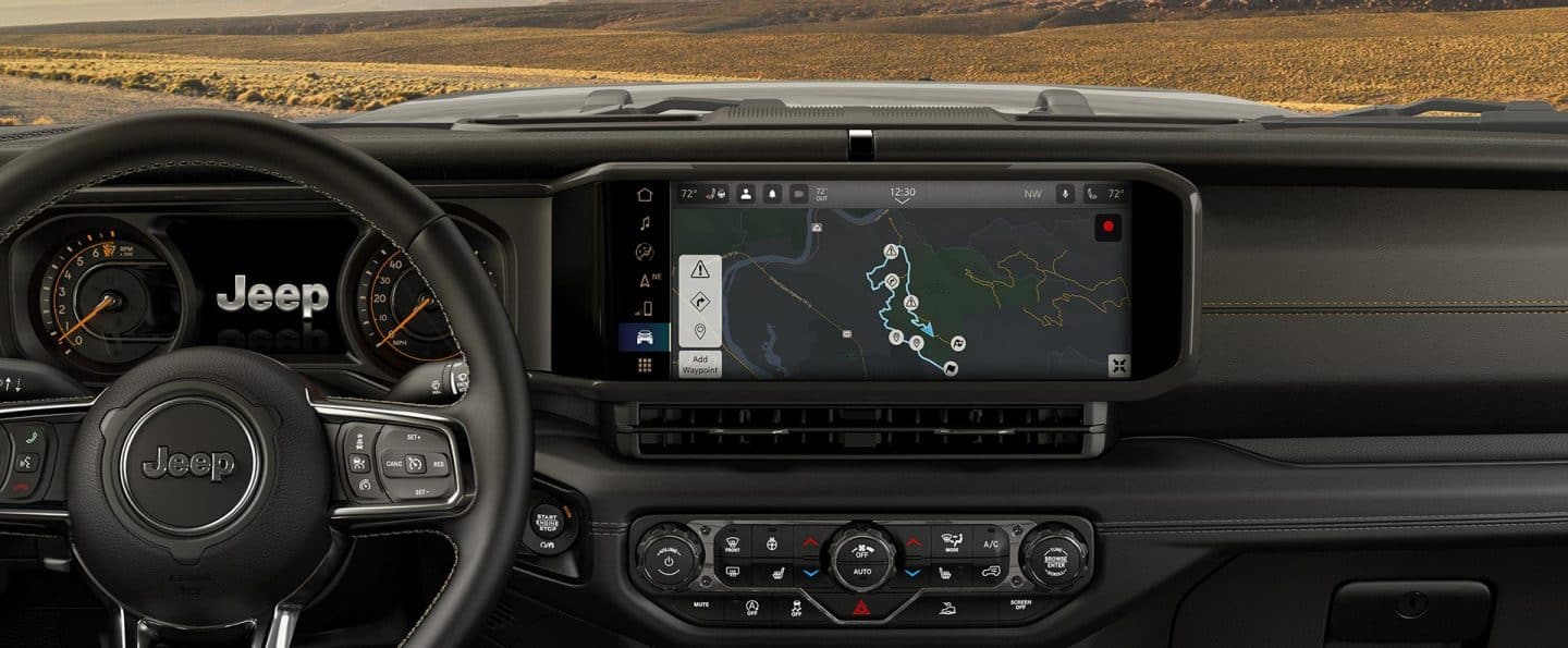 El volante, la pantalla digital en clúster y la Uconnect pantalla táctil del 2025 Jeep Wrangler con la pantalla táctil mostrando una de las guías todoterreno.