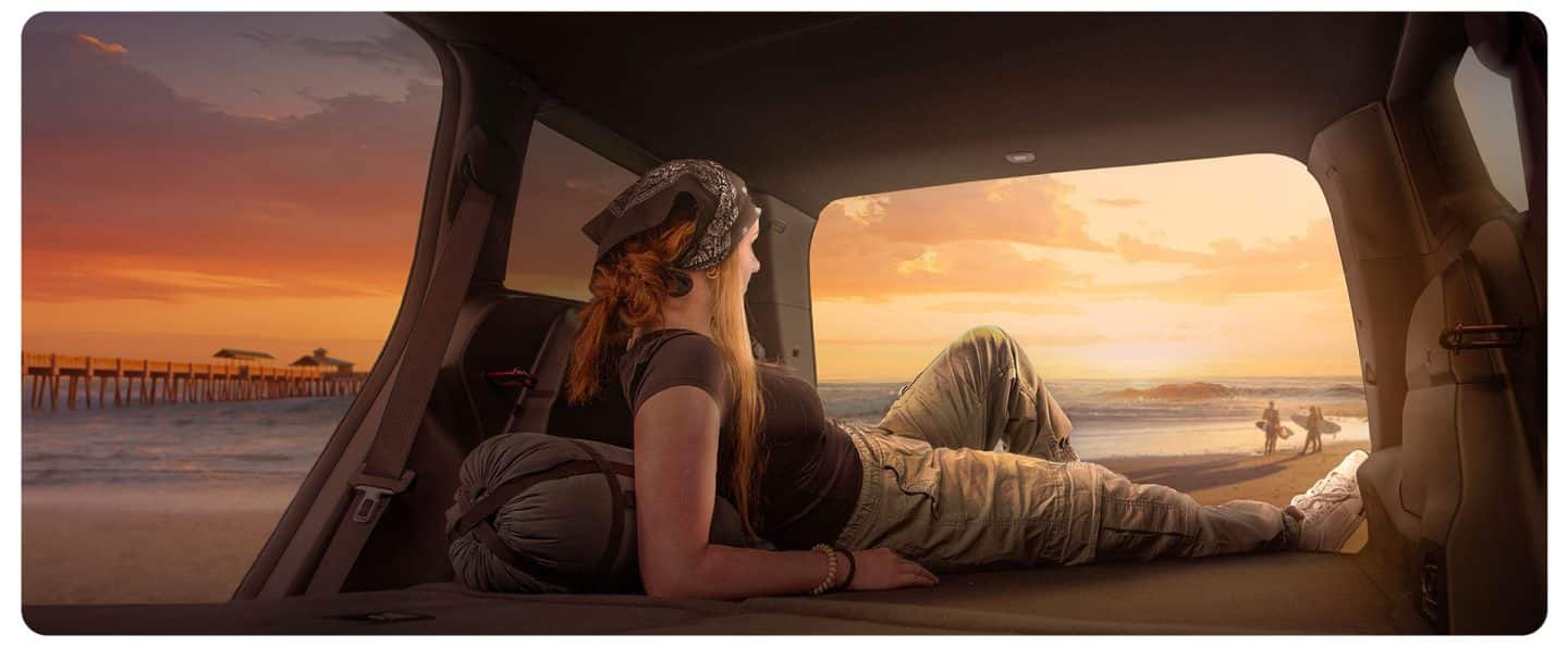 El interior de un Jeep® Cherokee 2026 con los asientos traseros plegados, la puerta trasera del lado del pasajero y la puerta trasera abiertos y una mujer recostada en el área de carga abierta.