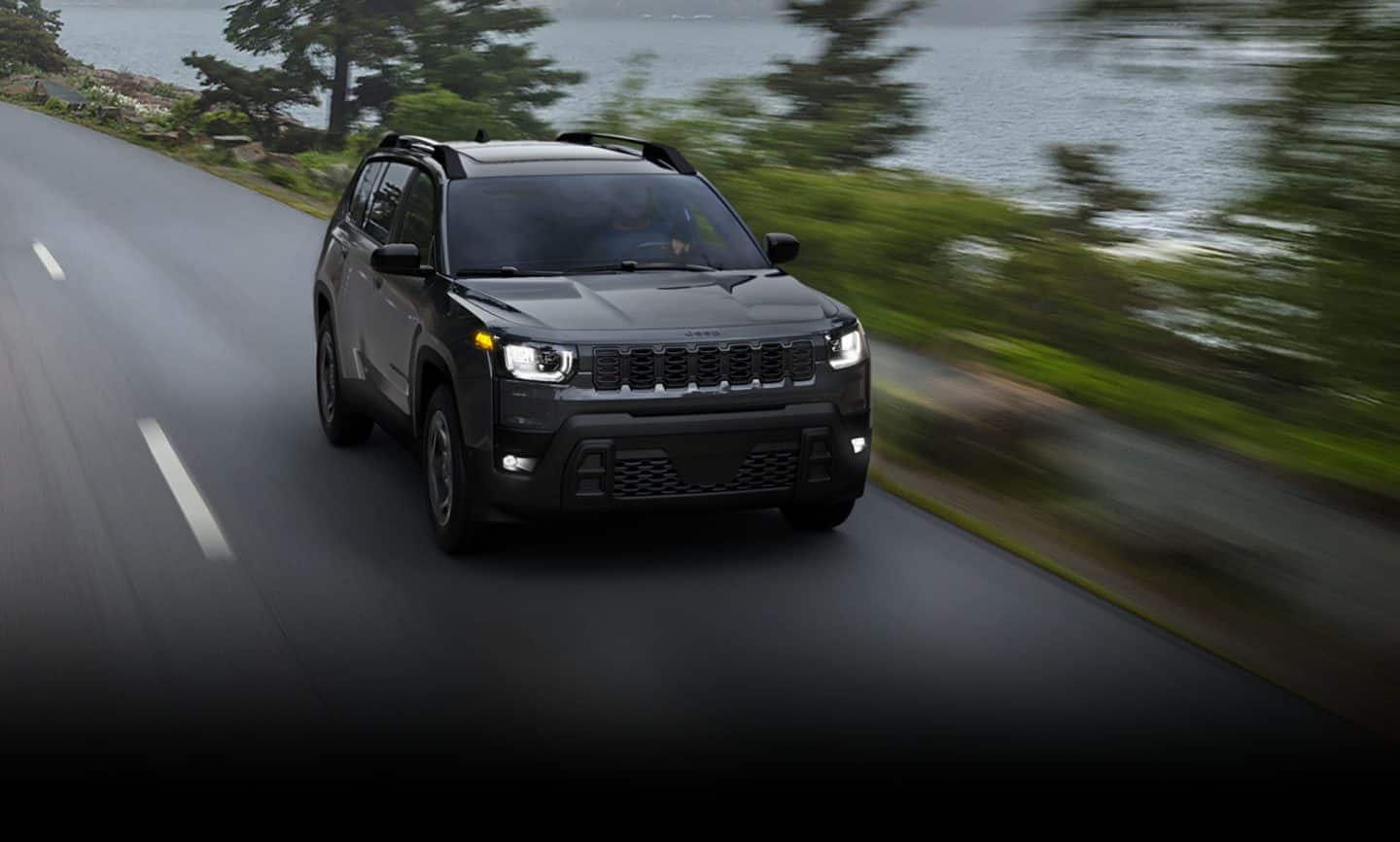 Un Jeep Cherokee Limited 2026 negro circulando por una carretera, junto a un lago. El fondo está borroso para indicar que el vehículo está en movimiento.