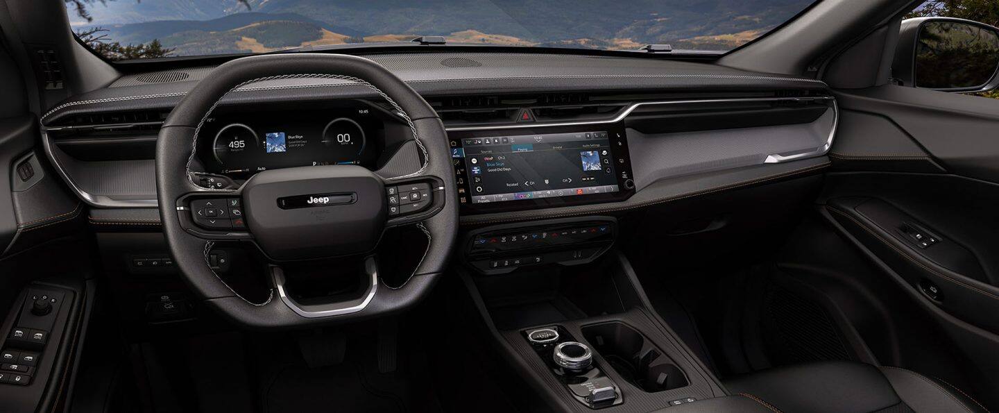 El área de los asientos delanteros del Jeep Cherokee 2026, con enfoque en el volante, la pantalla digital en el panel de instrumentos, la pantalla táctil Uconnect y los controles de la consola central.