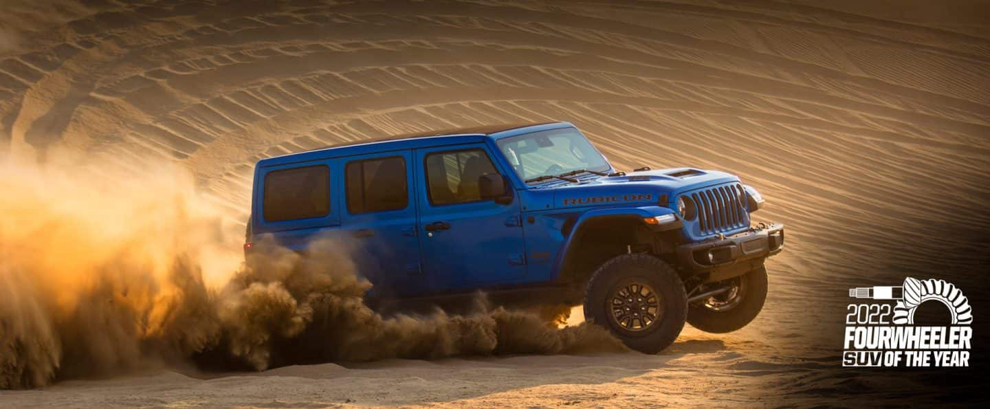 The 2021 Jeep Wrangler Rubicon 392 being driven on a sand dune, a cloud of dust coming from its wheels. Four Wheeler SUV of the Year award logo.