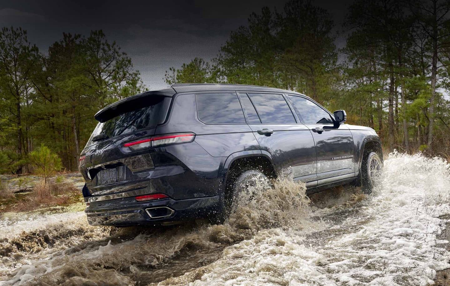 Una vista trasera de un Jeep Grand Cherokee L Altitude negro de 2023 mientras cruza un arroyo.