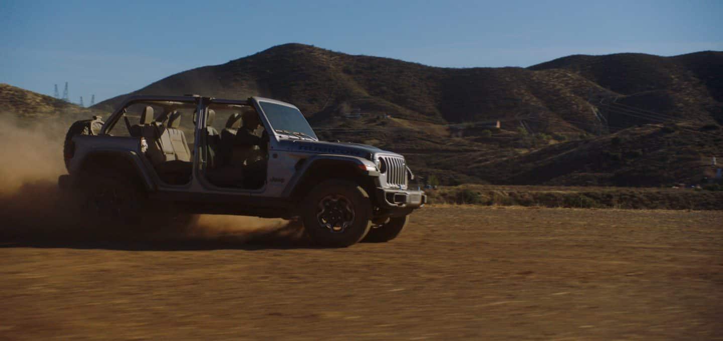 El Jeep Wrangler Rubicon 4xe 2023 circulando por la arena sin las puertas y con una nube de polvo que oculta las ruedas traseras.