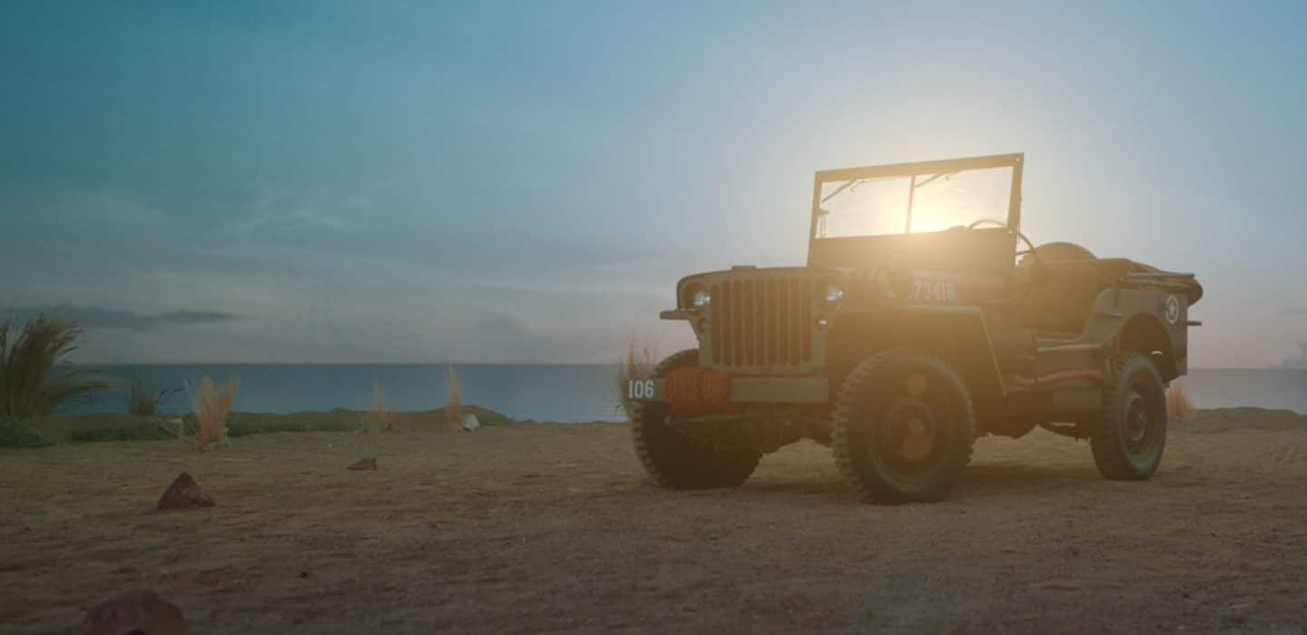 Un modelo clásico de Willys MB estacionado en una playa de arena.