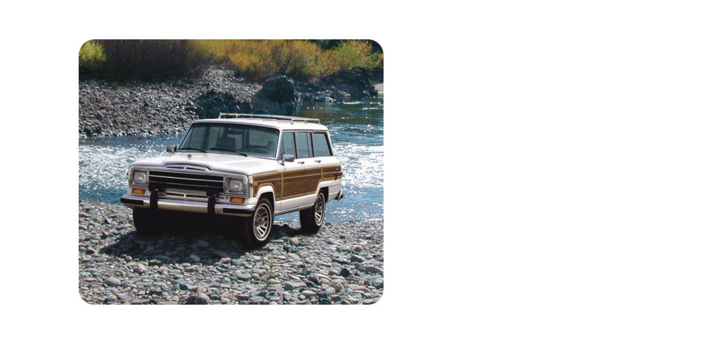 Un blanc Grand Wagoneer avec des panneaux latéraux en bois, sortant d’un ruisseau sur une plage rocheuse.