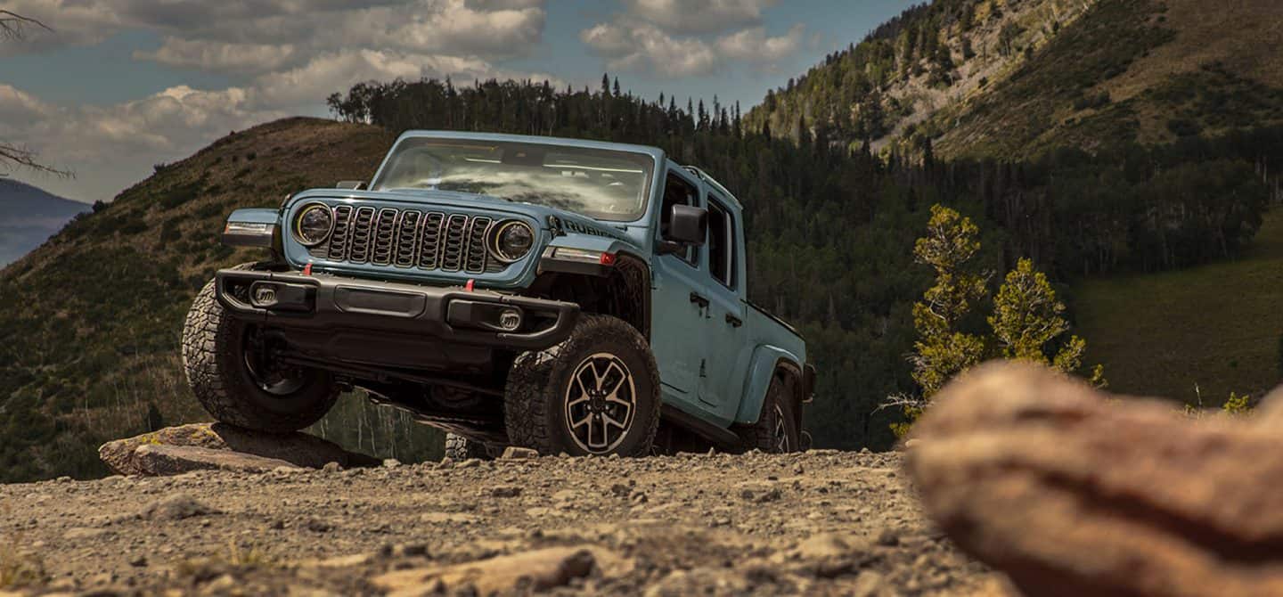 Un Jeep Gladiator Rubicon X 2025 roja ascendiendo por un sendero rocoso e irregular todoterreno con un Jeep Gladiator Rubicon X 2025 verde oliva detrás.