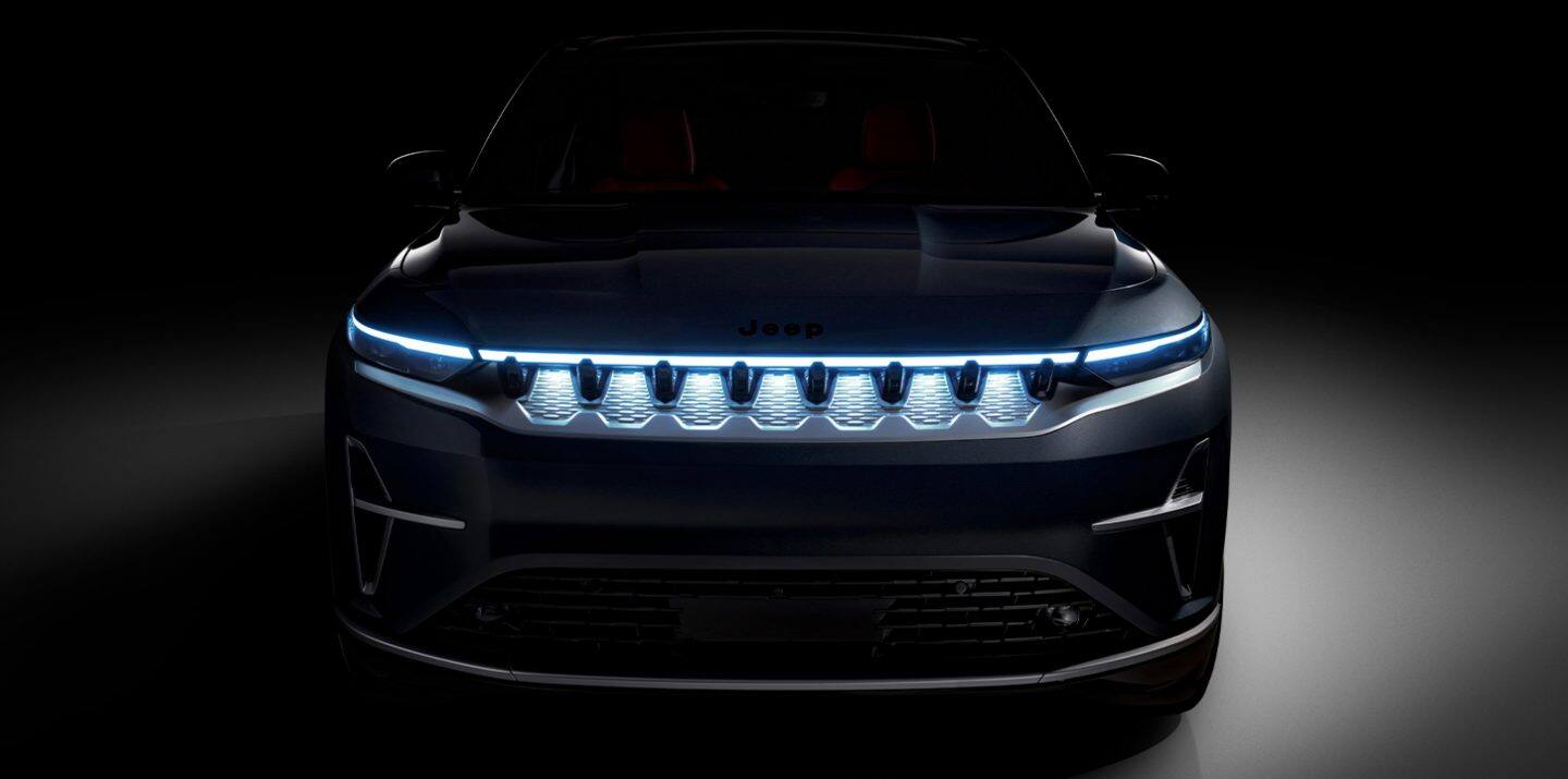 La parte delantera de un Jeep Wagoneer S Launch Edition 2025 negro con los faros delanteros encendidos, estacionado en un estudio oscurecido.