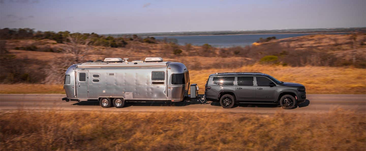  Un Jeep Wagoneer Carbide 2025 circulando por un camino campestre, acarreando un gran remolque de viaje.