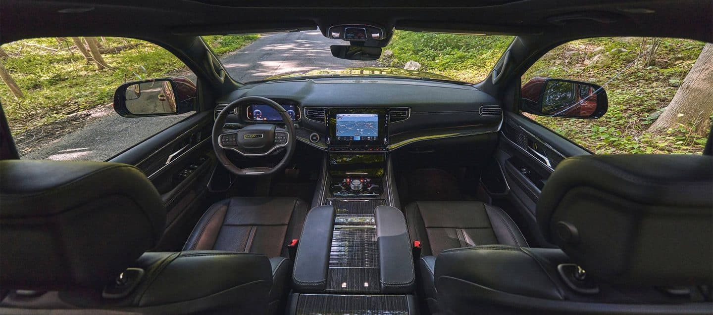 La primera fila de la cabina del Jeep Wagoneer Serie III 2025, con foco en los asientos, la consola central, el volante, la pantalla digital del grupo de instrumentos, los controles de la consola central con pantalla táctil Uconnect y el tablero.