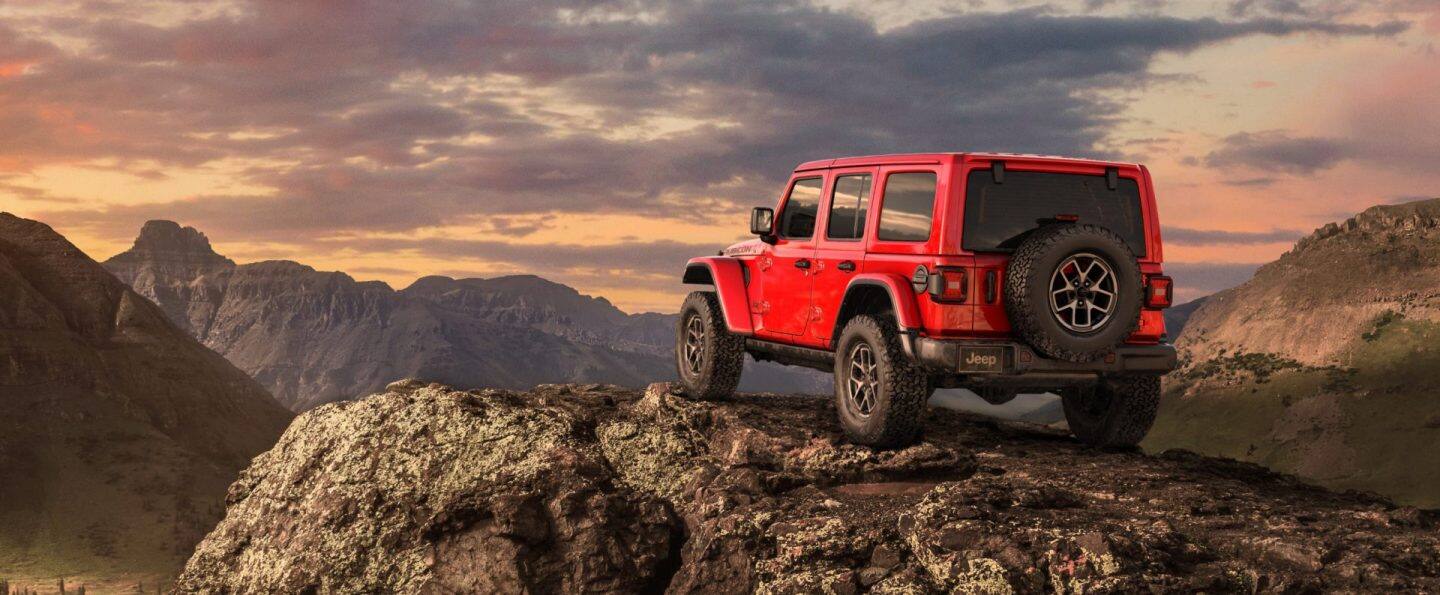 Un ángulo bajo de las aros, los neumáticos y la parte inferior del chasis de un Jeep Wrangler Rubicon X 4xe 2025 trepando un sendero rocoso, fuera de la carretera.