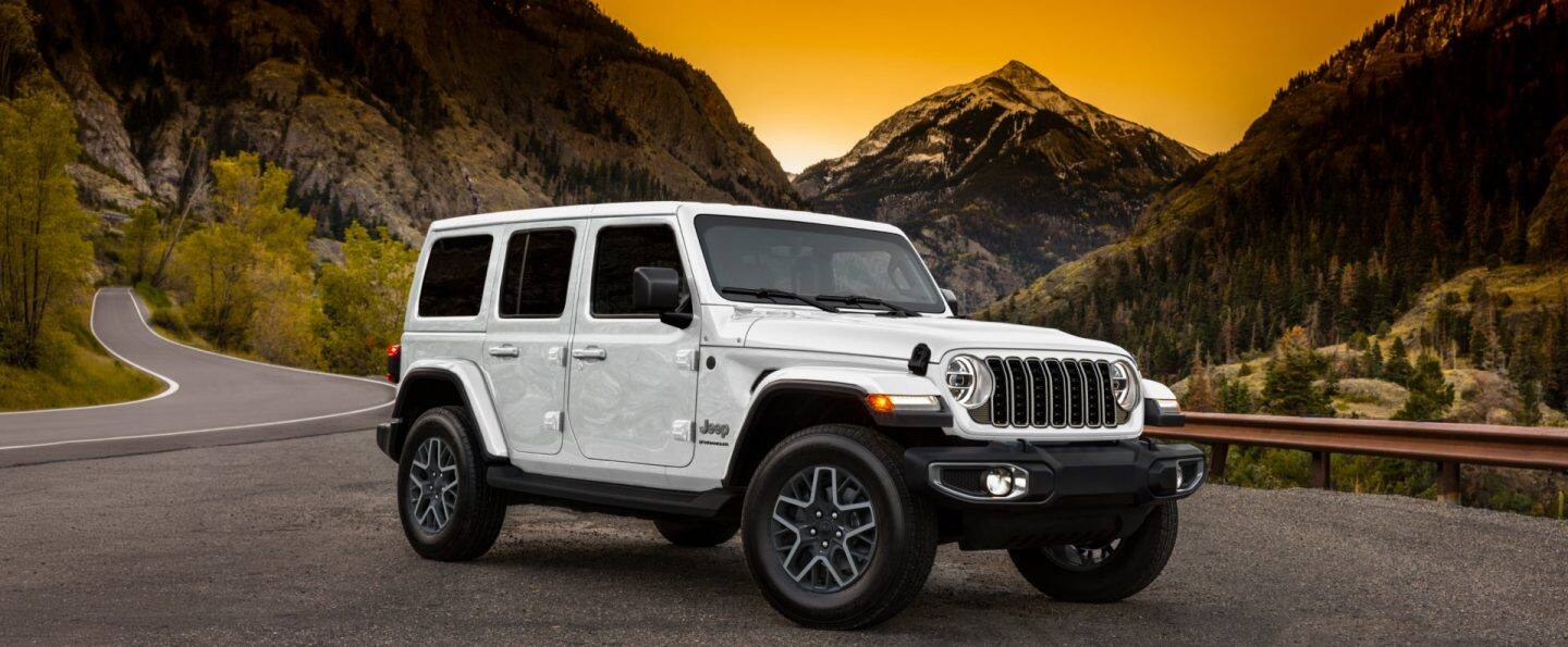 Perfil del lado del conductor de un Jeep Wrangler Rubicon X 4xe 2025 azul estacionado fuera de la carretera, con los neumáticos delanteros elevados en una formación rocosa. Wrangler.