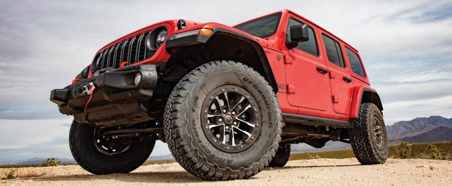Un Jeep Wrangler Rubicon 4xe 2025 rojo con las puertas y el techo extraídos, ingresando a un arroyo, fuera de la carretera. 