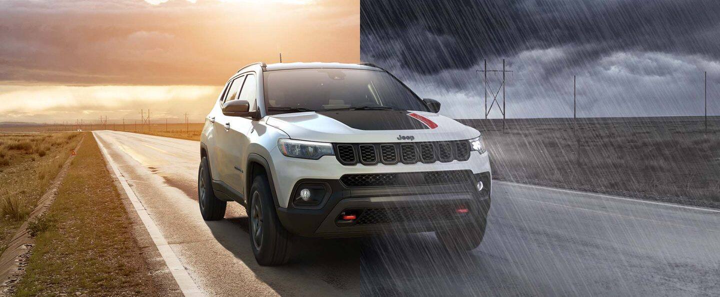 En una pantalla dividida, se muestra un Jeep Compass Trailhawk blanco de 2026 con una inserción negra en el capó, circulando por una autopista entre dos campos abiertos. A la izquierda, se ve un día despejado al atardecer; y a la derecha, un cielo oscuro y nublado descarga una fuerte lluvia sobre la autopista. 